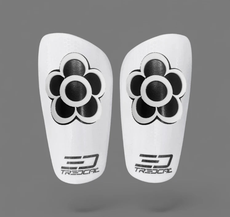 Pair of white shin guards with black floral design and TREDCAL branding.